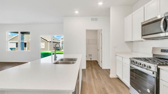 kitchen with sink, light hardwood / wood-style flooring, appliances with stainless steel finishes, a kitchen island with sink, and white cabinetry