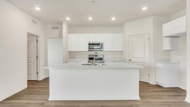 kitchen with appliances with stainless steel finishes, light hardwood / wood-style floors, an island with sink, and white cabinets