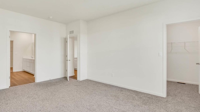 unfurnished bedroom featuring ensuite bathroom, a spacious closet, light colored carpet, and a closet