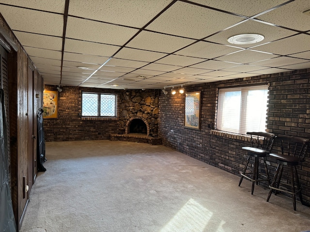 basement featuring brick wall, a stone fireplace, carpet, and a drop ceiling