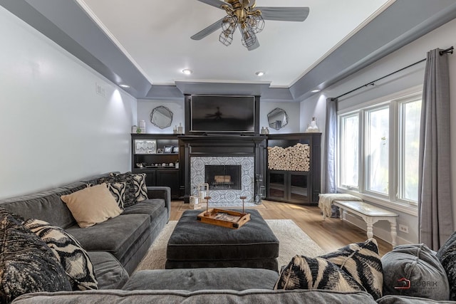 living area with wood finished floors, a ceiling fan, visible vents, a tiled fireplace, and crown molding