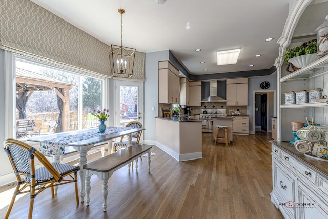 kitchen with dark wood-type flooring, high end stainless steel range oven, dark countertops, wall chimney range hood, and a chandelier