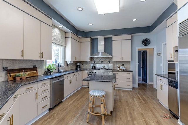 kitchen with a sink, light wood-type flooring, appliances with stainless steel finishes, and wall chimney exhaust hood