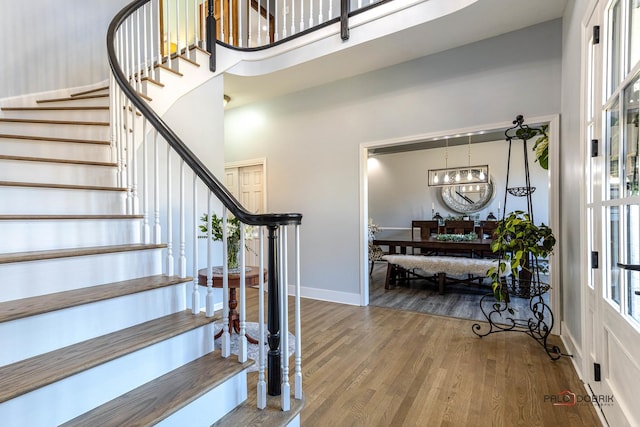 stairs with a notable chandelier, baseboards, a towering ceiling, and wood finished floors