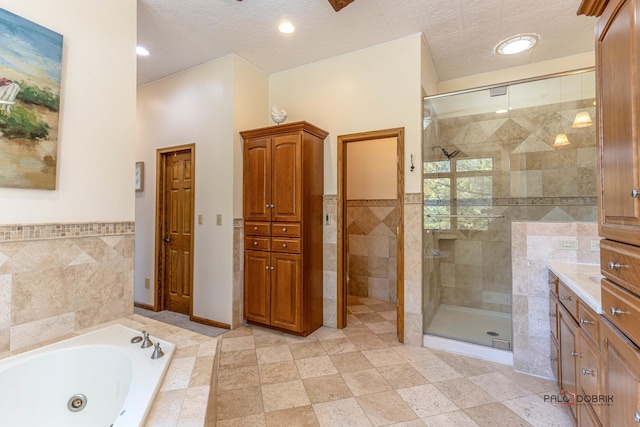 bathroom with a stall shower, a textured ceiling, tile walls, a tub with jets, and vanity