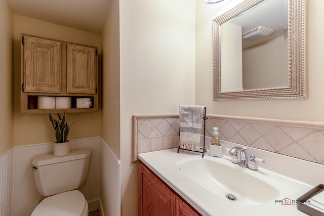 half bathroom with wainscoting, toilet, and vanity