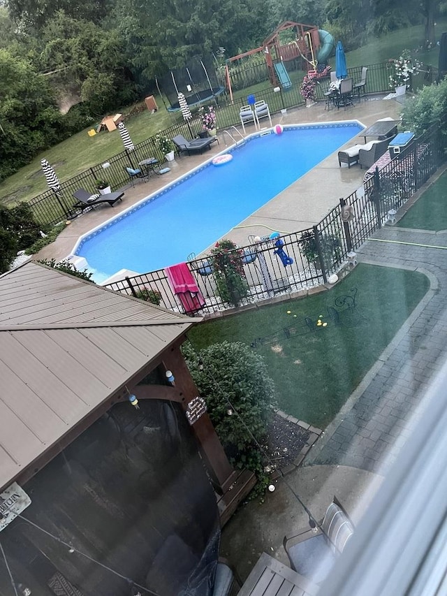 community pool with a patio area, playground community, a trampoline, and fence