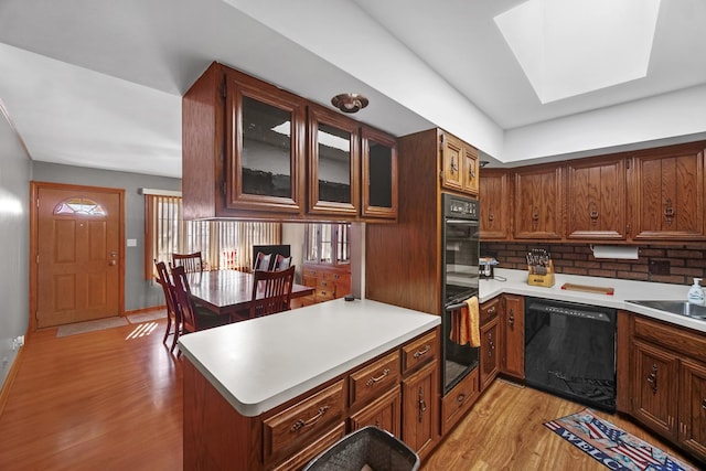 kitchen with light wood finished floors, a peninsula, black appliances, and light countertops