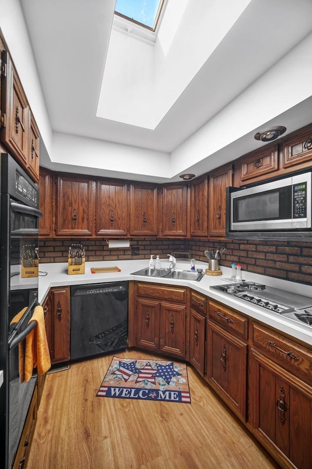 kitchen featuring black appliances, a sink, light wood-style floors, a skylight, and light countertops