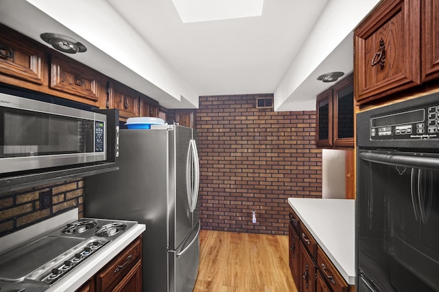 kitchen with stainless steel appliances, brick wall, light countertops, and light wood-style flooring