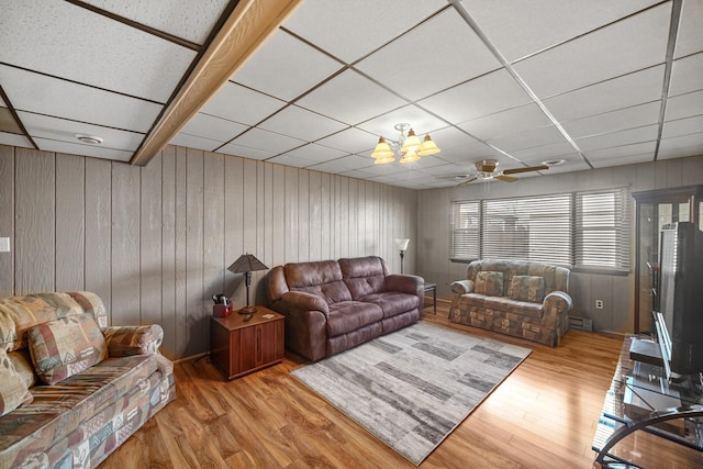 living area featuring light wood-style floors, wood walls, a drop ceiling, and ceiling fan