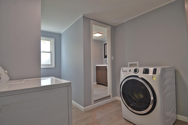 laundry room with crown molding, washer and clothes dryer, and light hardwood / wood-style flooring