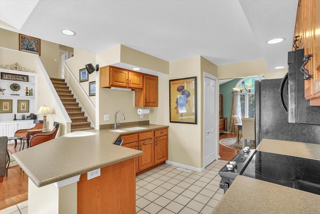 kitchen featuring brown cabinets, light countertops, a sink, a textured ceiling, and a peninsula