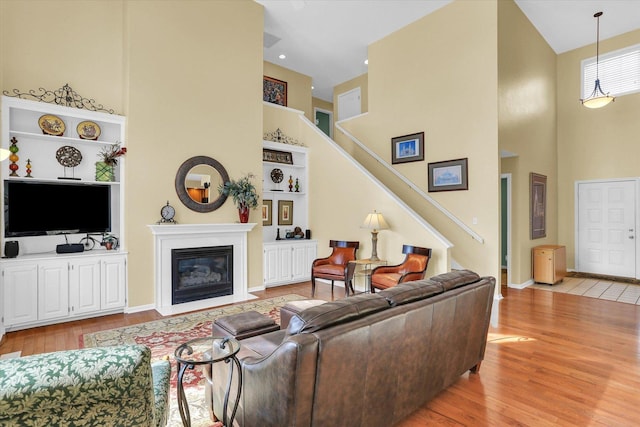 living area with a fireplace with flush hearth, a high ceiling, stairs, light wood-style floors, and built in shelves