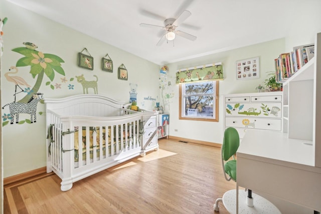 bedroom featuring hardwood / wood-style floors, a nursery area, and ceiling fan