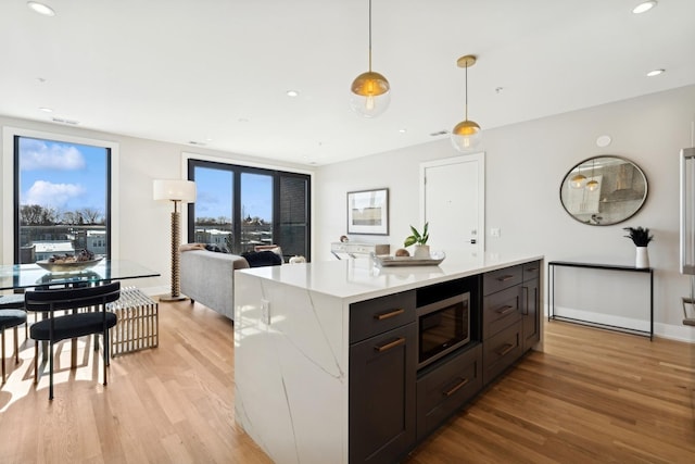 kitchen featuring stainless steel microwave, light wood-type flooring, hanging light fixtures, and a center island