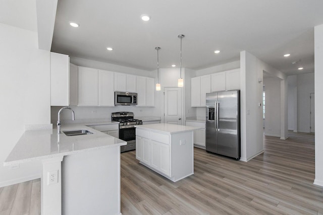 kitchen with sink, appliances with stainless steel finishes, white cabinets, a kitchen island, and decorative light fixtures