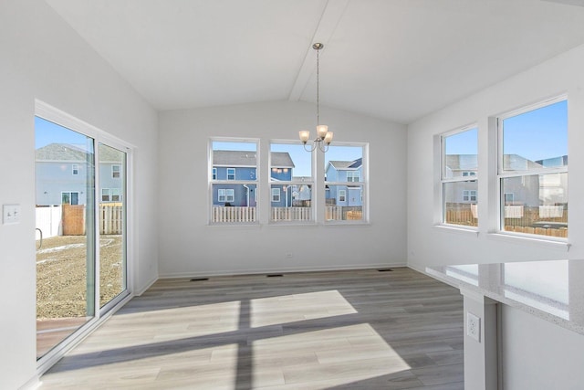 unfurnished dining area featuring an inviting chandelier, hardwood / wood-style flooring, vaulted ceiling, and plenty of natural light