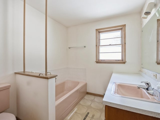 bathroom with a bath, vanity, toilet, and baseboards