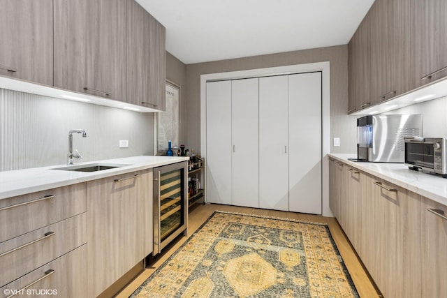 kitchen with light brown cabinets, beverage cooler, a sink, light wood finished floors, and modern cabinets