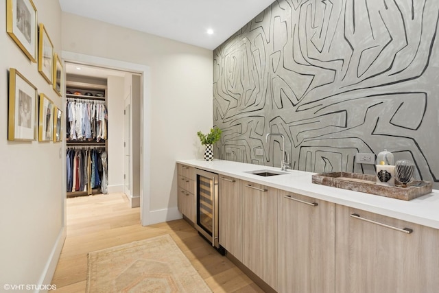 bar featuring light wood-type flooring, wine cooler, an accent wall, and a sink