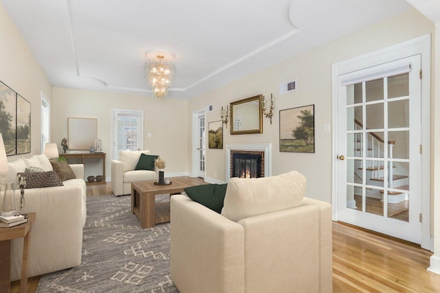 living room with a notable chandelier, wood finished floors, visible vents, baseboards, and a brick fireplace