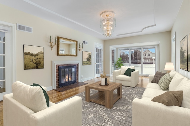 living area with a fireplace, a notable chandelier, visible vents, wood finished floors, and baseboards