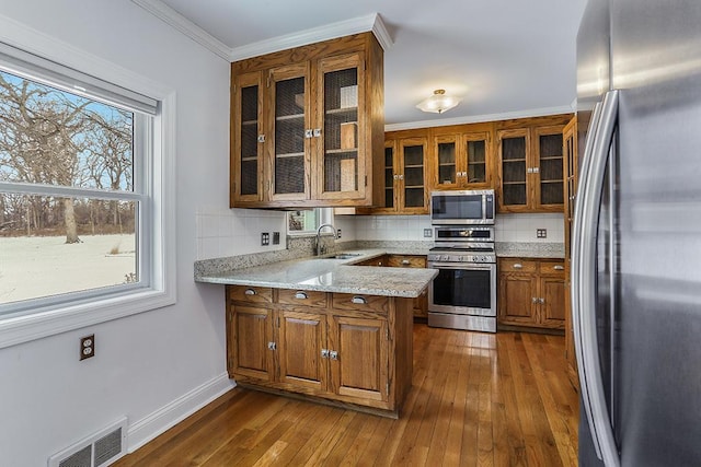 kitchen featuring tasteful backsplash, visible vents, brown cabinetry, appliances with stainless steel finishes, and a sink