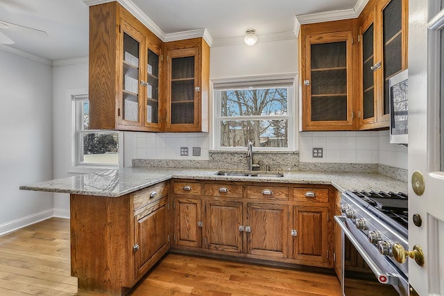 kitchen with brown cabinets, appliances with stainless steel finishes, ornamental molding, a sink, and a peninsula