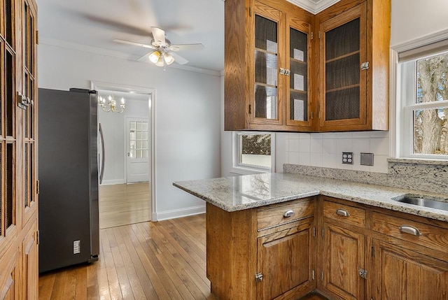 kitchen featuring decorative backsplash, hardwood / wood-style flooring, ornamental molding, brown cabinets, and freestanding refrigerator