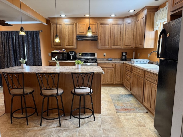 kitchen featuring decorative light fixtures, sink, light stone counters, and black appliances