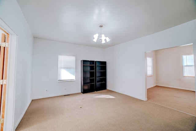 spare room featuring light colored carpet, visible vents, baseboards, and an inviting chandelier