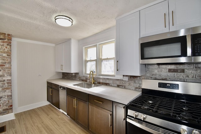 kitchen featuring stainless steel appliances, dark brown cabinets, light countertops, white cabinetry, and a sink