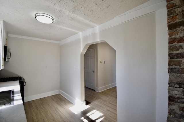 additional living space featuring arched walkways, a textured ceiling, baseboards, and wood finished floors