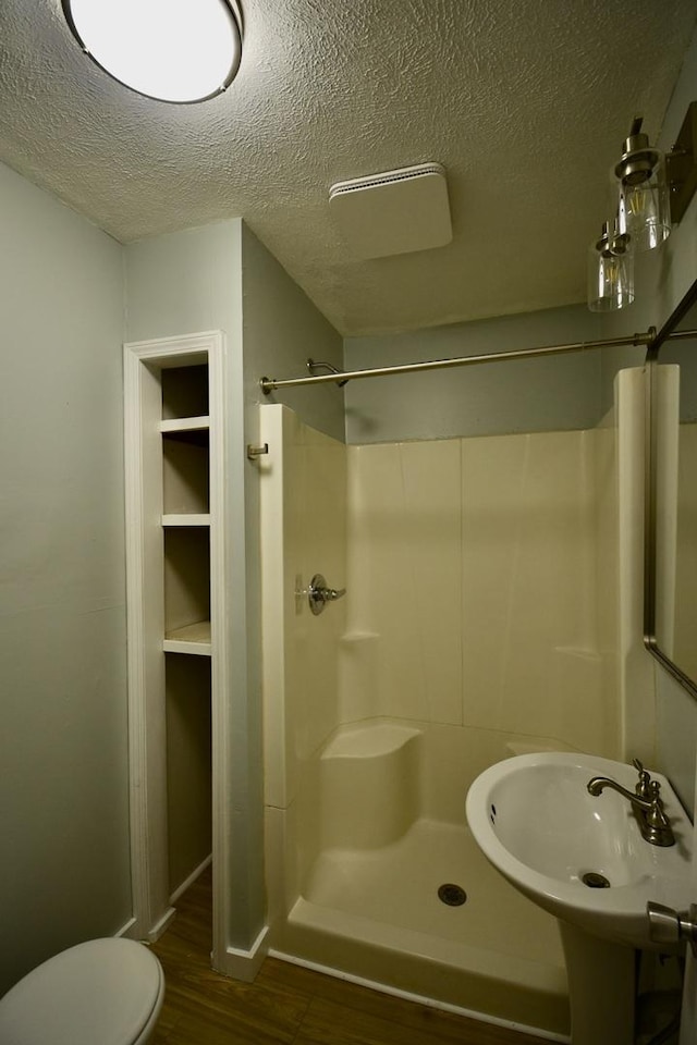 full bath with toilet, a sink, a shower stall, a textured ceiling, and wood finished floors