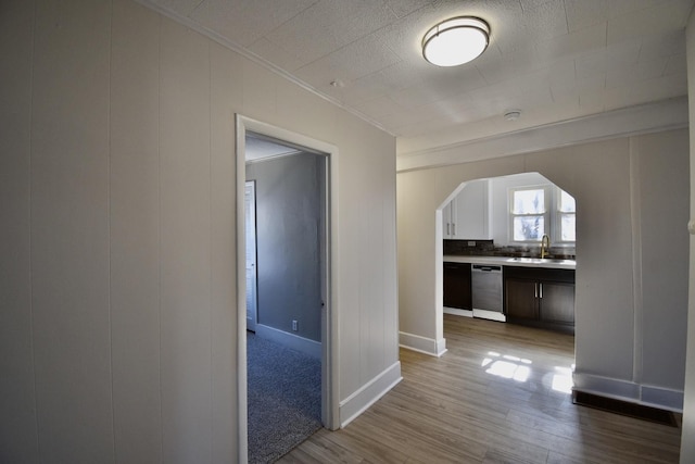 corridor featuring light wood finished floors, baseboards, arched walkways, ornamental molding, and a sink