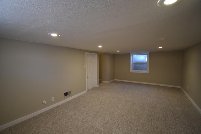 basement with a textured ceiling, carpet flooring, visible vents, and baseboards