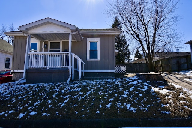 view of front facade featuring board and batten siding, covered porch, and fence