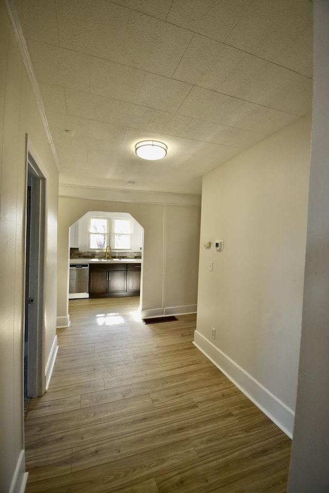 hallway with baseboards, arched walkways, a sink, and wood finished floors