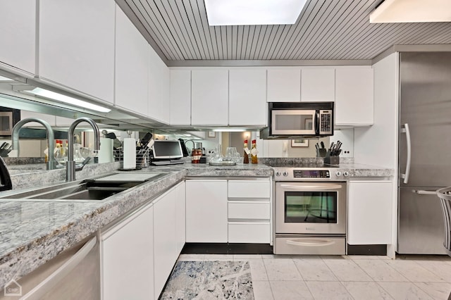 kitchen with appliances with stainless steel finishes, light stone countertops, sink, and white cabinets