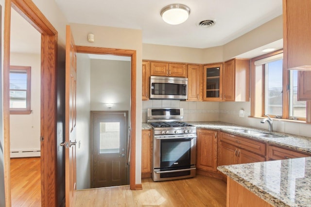 kitchen featuring light wood finished floors, tasteful backsplash, visible vents, appliances with stainless steel finishes, and a sink