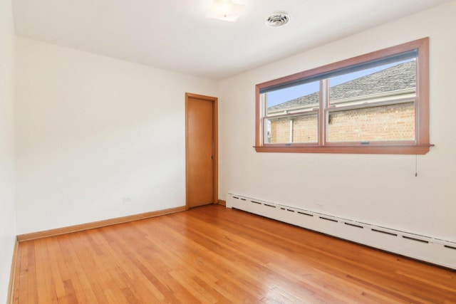 spare room featuring a baseboard heating unit, baseboards, visible vents, and light wood-style floors