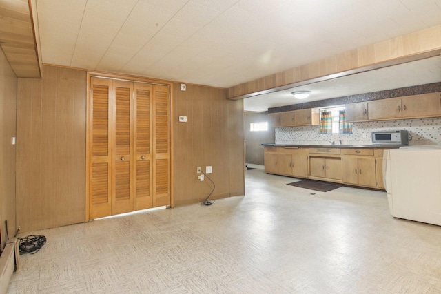 kitchen with white microwave, wooden walls, light floors, and washer / dryer