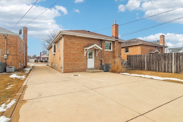 back of property featuring central AC unit, brick siding, fence, driveway, and a chimney