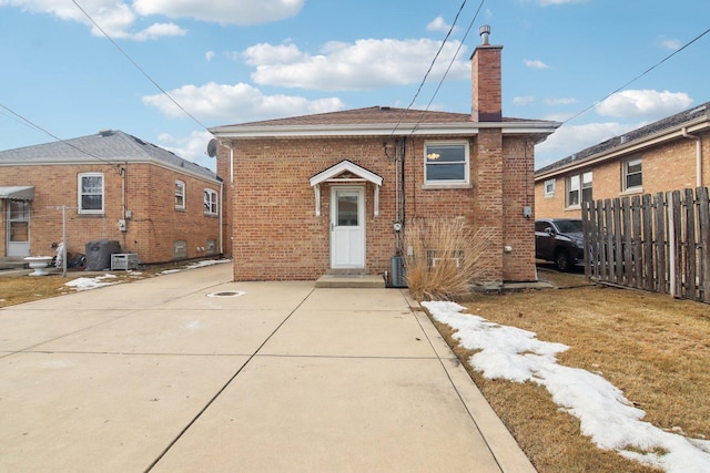 back of property with brick siding, fence, and a chimney