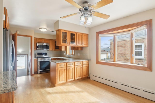 kitchen featuring stainless steel appliances, a baseboard radiator, light wood-style flooring, glass insert cabinets, and light stone countertops