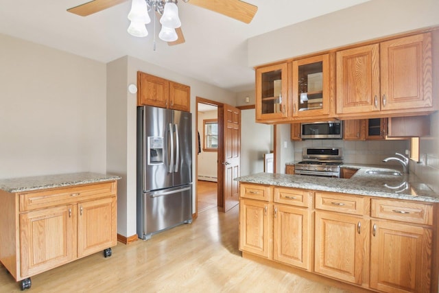 kitchen with stainless steel appliances, a sink, light wood-style floors, backsplash, and light stone countertops