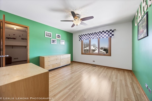 unfurnished bedroom with a closet, a walk in closet, ceiling fan, and light hardwood / wood-style flooring