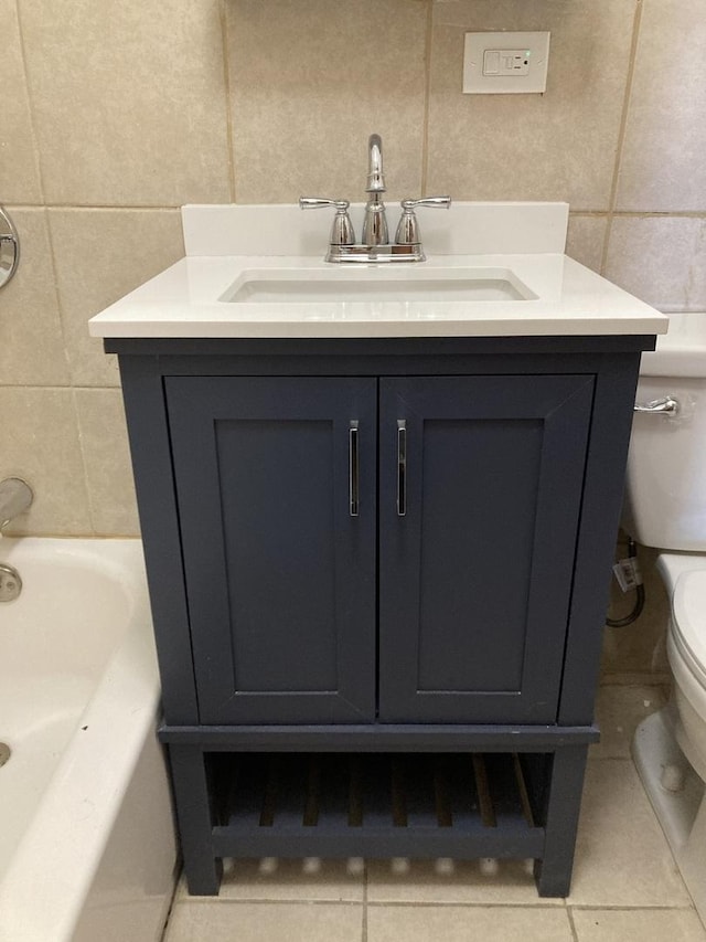 bathroom with tile walls, vanity, toilet, a bath, and tile patterned floors