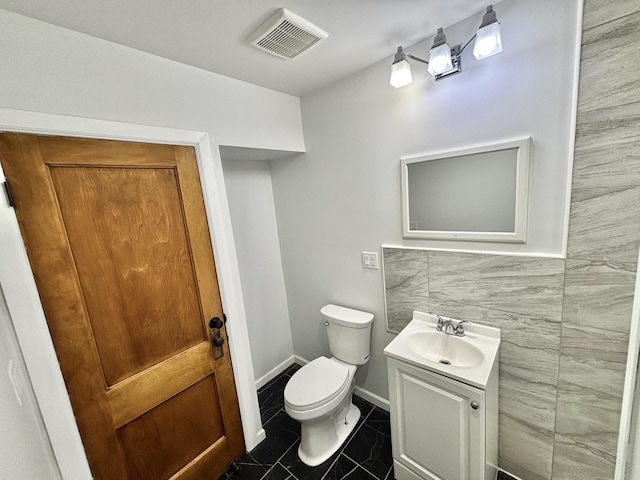 bathroom with vanity, toilet, and tile walls